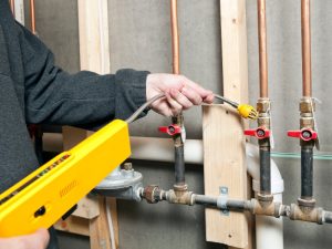 Technician inspecting old gas fittings with a gas leak detector to ensure safety in a home.