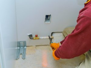 Worker using a wrench to tighten old gas fittings in a residential wall, ensuring safety and proper installation.