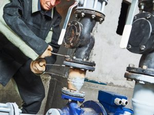 A plumber fixing a leaking valve to address low water pressure issues in a commercial building pipeline system.