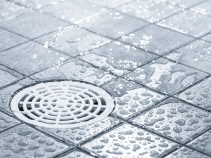 Wet tiled floor with a drain showing water droplets, highlighting potential causes of a noisy drain issue.