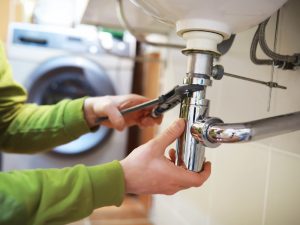 A person tightening a sink pipe with a wrench, demonstrating a repair for a noisy drain problem.