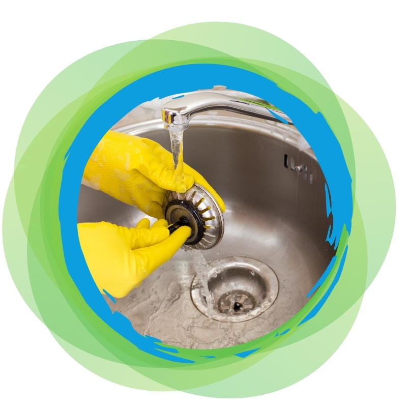 Cleaning a kitchen blocked drain strainer with yellow gloves under running water to remove debris and prevent clogging.