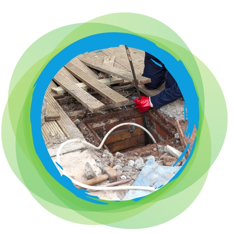 A plumber clearing a blocked drain by working on a hole in the ground, demonstrating professional drain repair services.