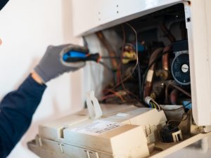 A professional repairing an electric water heater's internal components, checking wiring before trying to reset water heater.