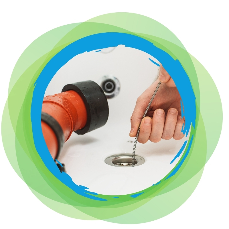 Hand using plumbing snake to clear bathtub blocked drain near red drainage pipe.