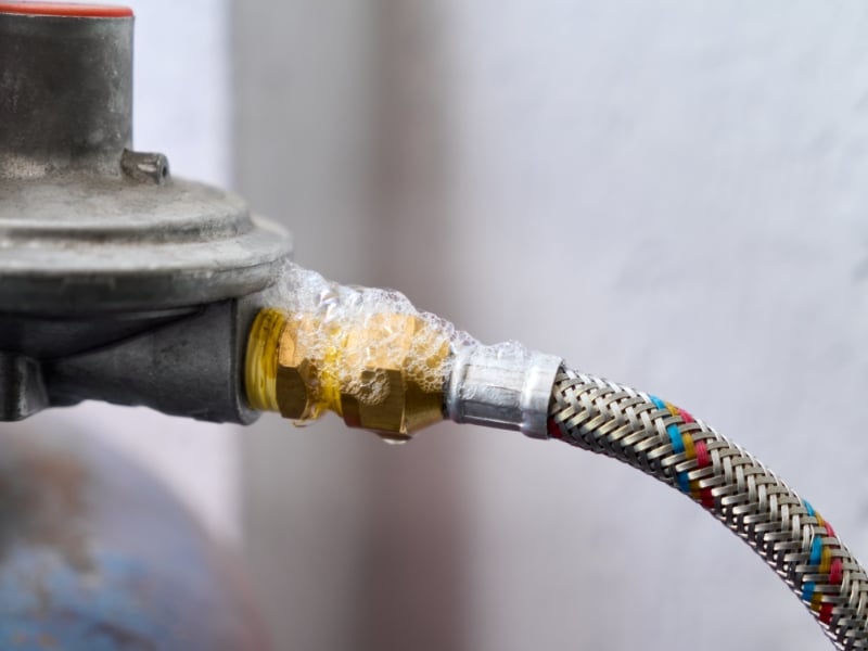 bubbles reveal a gas leak from failing gas pipe fittings connected to a regulator, indicating dangerous leakage.