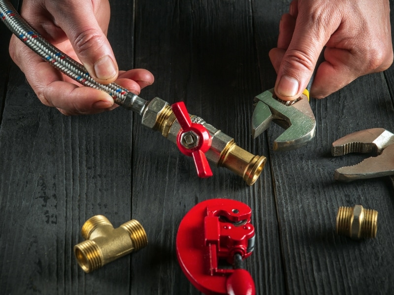 A person repairs failing gas pipe fittings with tools, tightening a metal connector on a gas hose.