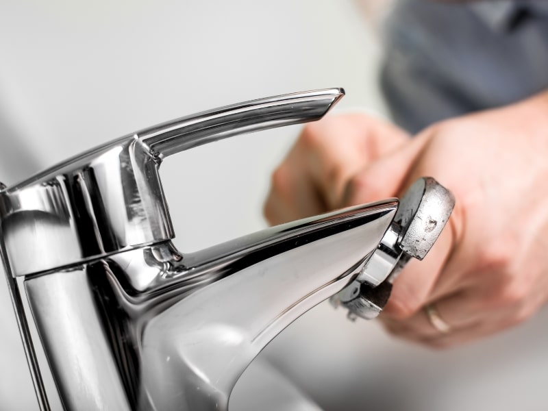 Plumber using wrench for fixing a leaking tap with chrome finish in a bathroom setting