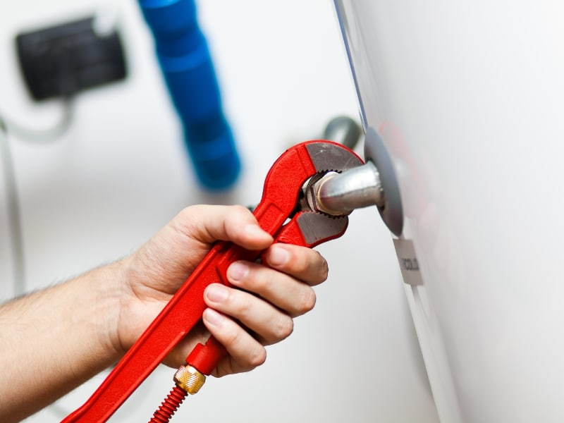 Routine hot water maintenance with wrench on water heater pipe fitting.