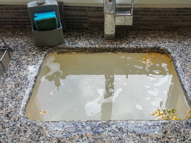 kitchen blocked drain with stagnant dirty water and food scraps in granite sink