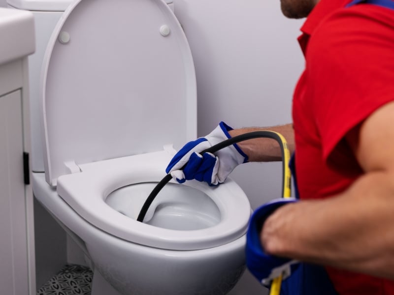 Blocked toilet plumbers using drain snake to clear stubborn toilet blockage.